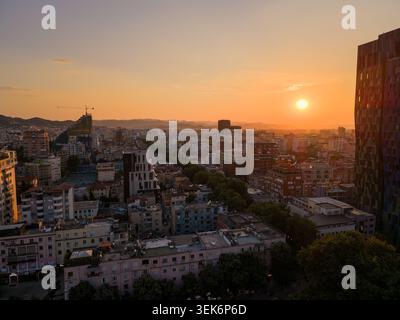 Blick aus der Vogelperspektive auf die Skyline von Tirana bei Sonnenuntergang mit goldenem Licht über Dächern und entfernten Bergen Tirane, Tirana County, Albanien. Stockfoto