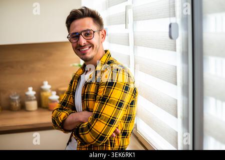 Porträt eines fröhlichen jungen Mannes in seiner Küche. Er schaut in die Kamera und lächelt. Stockfoto