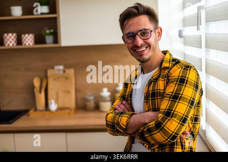 Porträt eines fröhlichen jungen Mannes in seiner Küche. Er schaut in die Kamera und lächelt. Stockfoto