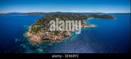 Blick aus der Vogelperspektive auf den Leuchtturm Faro di Punta Sardegna auf einer felsigen Halbinsel, umgeben von türkisfarbenem mediterranem Wasser und zerklüfteten Hügeln in Palau, Sardegna Stockfoto