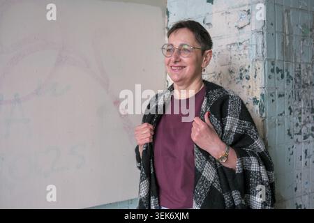 Eine fröhliche Frau posiert warm in einem stilvollen Outfit inmitten rustikaler Wände. Stockfoto