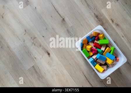 Blick von oben auf farbenfrohe Holzklötze, die in einer weißen Plastikbox auf hellem Holzboden angeordnet sind und einen Kopierraum bieten Stockfoto