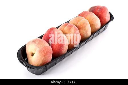 Flache Pfirsiche, auch bekannt als Doughnut Pfirsiche, in einer Reihe auf einem schmalen schwarzen Kunststofftablett. Weißer Hintergrund. Stockfoto