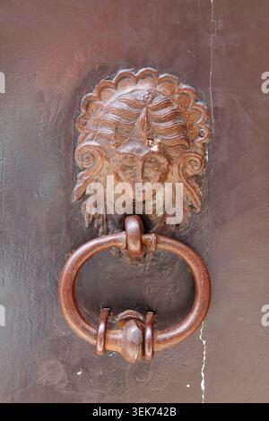 Vintage-Türklopfer mit einem Gesichtsdesign aus Bronze, befestigt an einer dunklen Holztür, die detaillierte Handwerkskunst und Textur hervorhebt Stockfoto
