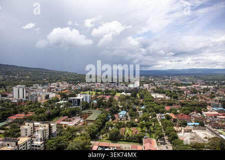 Aus der Vogelperspektive auf die Skyline der Stadt und die üppigen grünen Bäume unter einem dramatischen bewölkten Himmel in Nakuru, Nakuru County, Kenia. Stockfoto