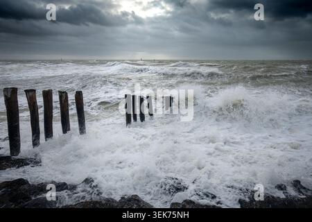 Eine dramatische Küstenszene in Westkapelle, Niederlande, mit turbulenten Meereswellen, die gegen verwitterte Holzpfeiler krachen. Stockfoto