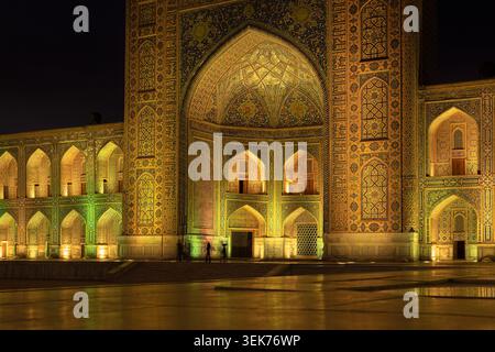 Beleuchtete Tilla-Kari-Madrasah-Fassade am Registan Square in Samarkand bei Nacht mit komplizierten Fliesen und goldener Beleuchtung. Ideal für Reiseveröffentlichungen Stockfoto