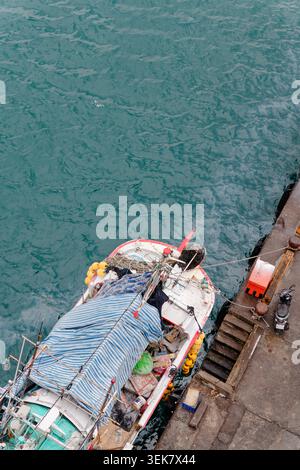 Yilan, Taiwan - 31. März 2025: Kleines Fischerboot mit blau gestreifter Plane an der Nanfangao Pier Steppe, von oben gesehen mit blauem Hafenwasser. Stockfoto