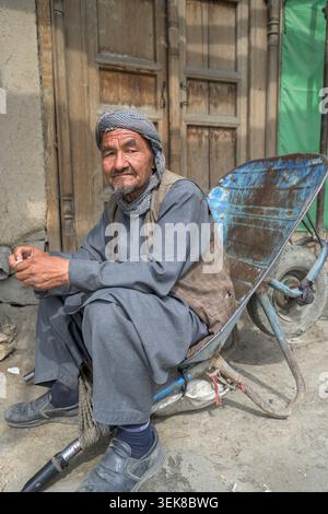 Älterer Mann in traditioneller Kleidung und Turban, der auf einer Schubkarre auf einer Straße sitzt Stockfoto