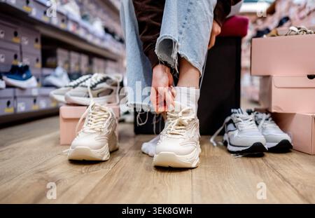 Frau in Einem Geschäft passt zu lässigen Sportschuhen, während Eine Nahaufnahme Füße und Laufschuhe zeigt Stockfoto