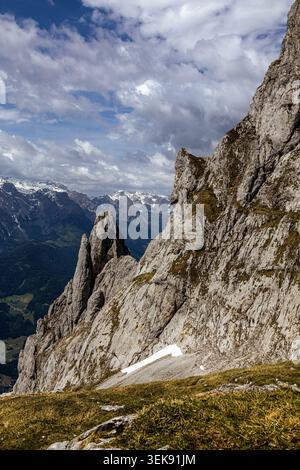 Ein atemberaubender Blick auf eine zerklüftete alpine Landschaft mit dramatischen Felsformationen und schneebedeckten Gipfeln unter bewölktem Himmel. Üppige grüne Vegetation Co Stockfoto