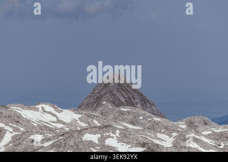 Ein atemberaubender Blick aus der Vogelperspektive fängt einen zerklüfteten Berggipfel mit schneebedeckten Hängen ein und erhebt sich über eine Landschaft aus felsigem Gelände. Der Gipfel ist scharf Stockfoto