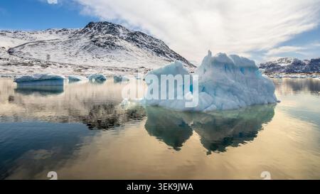 Blaue Eisbildung spiegelt sich im stillen Küstenwasser unter schneebedeckten Bergen in einer ruhigen Winterlandschaft in der Nähe von Narsaq, Kujalleq, Grönland Stockfoto