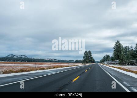 Malerische Winterstraße, die sich durch eine schneebedeckte Berglandschaft unter bewölktem Himmel erstreckt Stockfoto