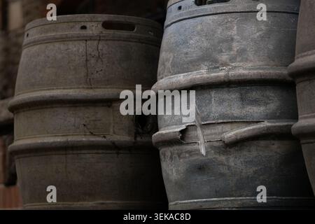 Verwitterte Bierfässer aus Aluminium, die vor einer Brauerei gestapelt sind und bei schlechten Lichtverhältnissen industrielle Abnutzung und Textur zeigen. Stockfoto