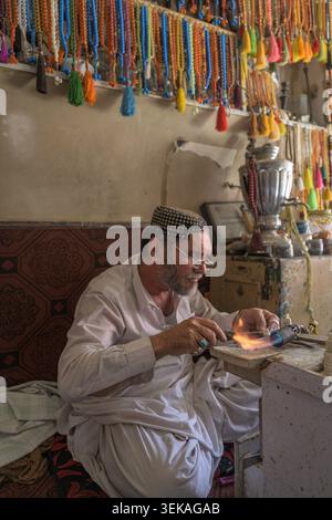 In einer traditionellen Juwelierwerkstatt, umgeben von bunten Perlen, werden in einer Handwerkstatt mit einer Taschenlampe Gebetskegeln sorgfältig hergestellt. Stockfoto
