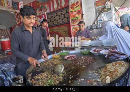Junger Mann, der an einer großen Pfanne steht und frisches Fleisch und Gemüsegerichte für Kunden auf einem geschäftigen Straßenmarkt zubereitet. Stockfoto