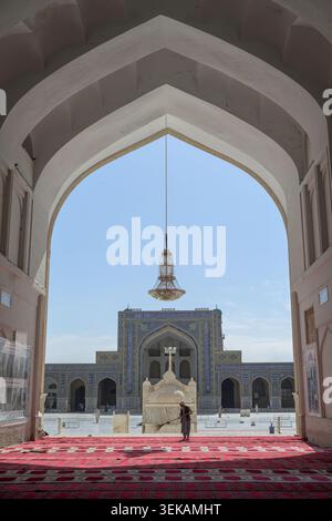 Mann, der den roten Teppich im historischen Herat großen Moschee-Innenhof fegt, eingerahmt von einem alten Bogengang. Stockfoto