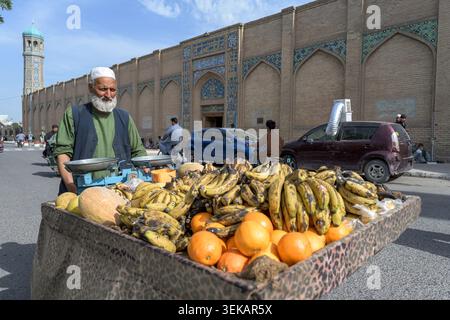 Straßenverkäufer, der mit einem Obstwagen mit Bananen, Orangen und Melonen vor der großen Moschee von Herat steht. Stockfoto