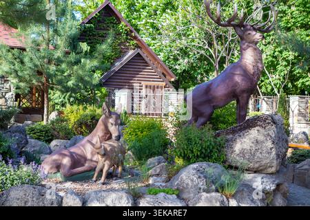 Hirschskulpturen von Hirsch, Hirsch und Rehkitz in einem Landschaftsgarten neben einem rustikalen Holzhaus Stockfoto