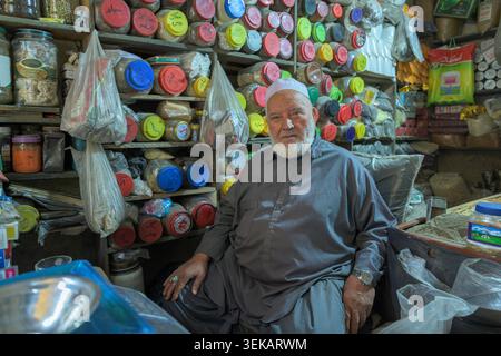 Senior Merchant betreibt ein traditionelles Gewürzgeschäft auf dem herat Basar, umgeben von Gläsern und Taschen mit verschiedenen Zutaten. Stockfoto