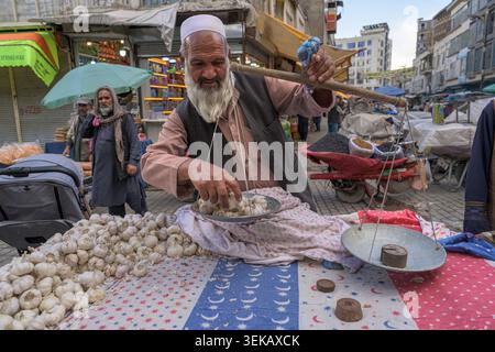 Händler, der frischen Knoblauch auf einer Waage auf einem belebten Straßenbasar in Kabul wiegt. Stockfoto