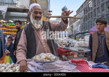 Mann wiegt Knoblauchzwiebeln mit einer Waage an einem geschäftigen Marktstand in Kabul. Stockfoto