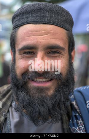 Afghane lächelt in die Kamera, trägt einen dunklen Bart und eine gemusterte Wollmütze, zeigt Glück. Stockfoto