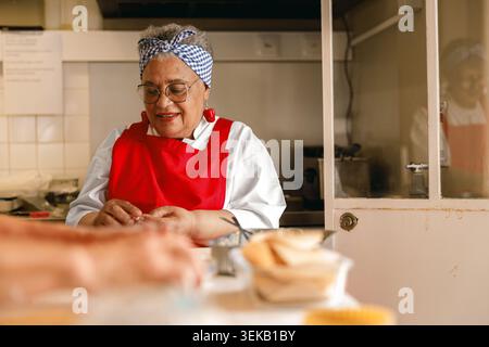 Senior Black Woman Küchenchef, der in der professionellen Küche Speisen zubereitet und eine aktive Langlebigkeit bietet Stockfoto