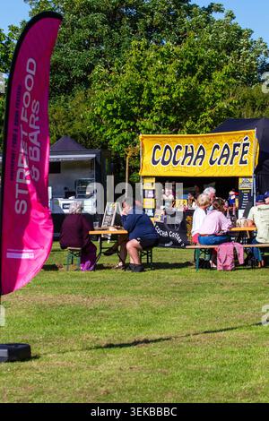 Ein Outdoor-Event mit Cocha Café Catering-Stand Sitzgelegenheiten an Holztischen auf einer Rasenfläche. Southport, UK. Stockfoto