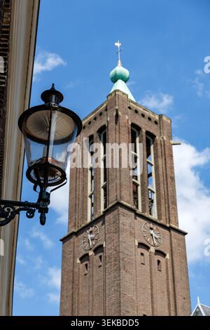 Hoher gemauerter Kirchturm mit Uhr und grüner Kupferkuppel neben einer antiken Laterne. Stockfoto