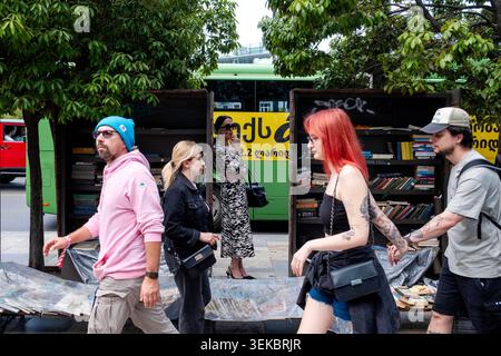 Eine Gruppe von Leuten läuft an einem Straßenverkäuferstand vorbei, während eine Frau in Tiflis, Georgia, raucht. Stockfoto