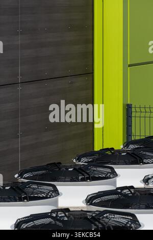 Industrielle Außenklimaanlagen befinden sich neben einem Geschäftsgebäude mit hellgrünen Wandpaneelen und Metallzaun. Stockfoto
