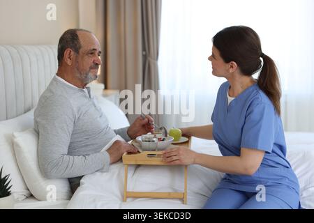 Die Pflegekraft frühstückt einem älteren Mann zu Hause im Bett Stockfoto