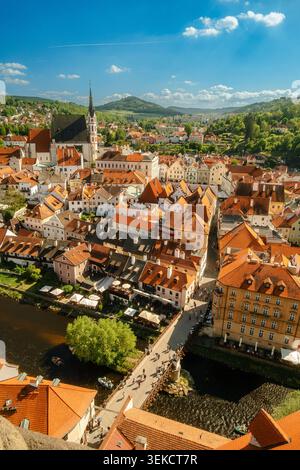 Aus der Vogelperspektive auf eine europäische Stadt am Fluss mit roten Dächern, Kirchturm und grünen Hügeln unter blauem Himmel Stockfoto