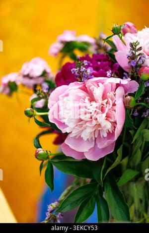 Vertikale Makroaufnahme einer blühenden üppigen rosafarbenen Pfingstrosenblüte in einem floralen Arrangement vor einem verschwommenen warmgelben Hintergrund mit negativem Raum auf dem l Stockfoto