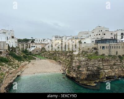 Polignano A Mare in Apulien, Italien, verfügt über Küstenklippen mit weiß getünchten Gebäuden auf dem Dach. Eine Steinbrücke über einen schmalen Kiesstrand, Stockfoto