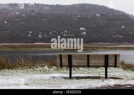 Blick auf eine Bank im Freien mit Blick auf einen Wald auf einem Hügel mit einem Fluss und Schnee auf dem Boden Stockfoto