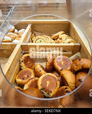 In einer Holzbackkiste finden Sie verschiedene Backwaren wie Schokoladenchips, Zimtrollen und Donuts. Kunden besuchen den Schalter, um ihre Favoriten auszuwählen Stockfoto