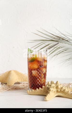 Ein Glas kalter Cuba Libre Cocktail, Seesterne und Palmenblätter auf weißem Hintergrund Stockfoto