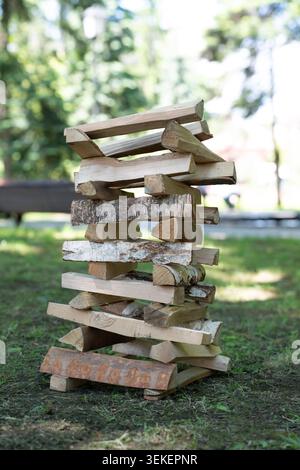 In einem Sommerpark gestapelte Holzscheite im turmförmigen Jenga-Stil auf grünem Gras Stockfoto