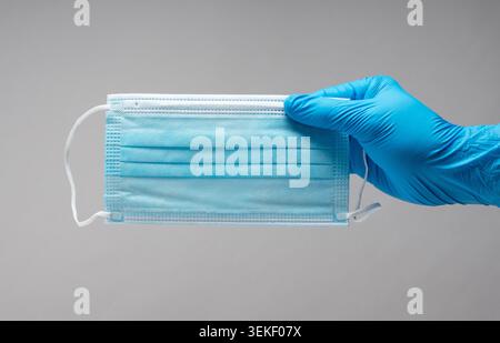 Handschuhe, die blaue Einweg-chirurgische Gesichtsmaske auf grauem Hintergrund halten Stockfoto