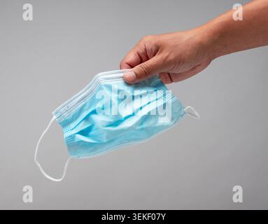 Menschliche Hand, die einzelne chirurgische Einweg-Gesichtsmaske auf grauem Hintergrund hält Stockfoto