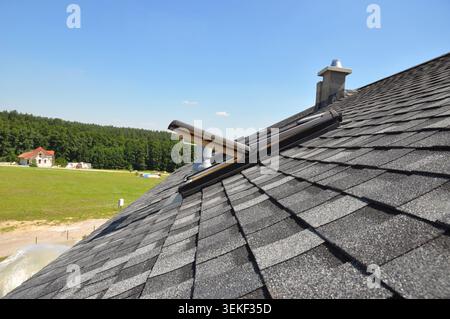 Asphaltschindeldach mit offenem Dachfenster und unvollendetem Dachschornstein Stockfoto