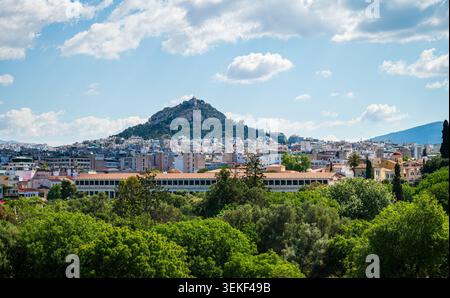 Die Skyline von Athen um den Lycabettus-Hügel durch die üppig grünen Baumkronen der antiken Agora Stockfoto