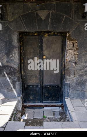 Alte, verwitterte Doppeltür in Steinmauer. Die Tür zeigt Zeichen von Alter und Vernachlässigung Stockfoto