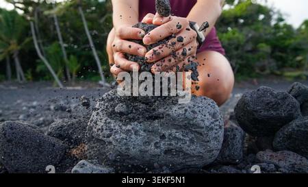 Hintergrund und Textur Foto einer nicht erkennbaren Person zerquetscht ein poröses Lavastein gegen vulkanische Steine und schickt schwarzen Kies nach draußen. Stockfoto