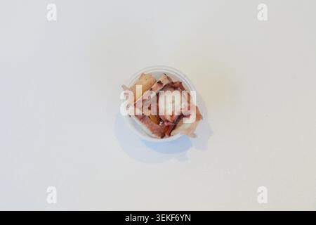 In Scheiben geschnittene Tintenfischstücke in einem kleinen Plastiktopf auf weißem Hintergrund für die Zubereitung von Meeresfrüchten in einer Poke-Schüssel. Stockfoto