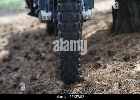 Nahaufnahme der Vorderansicht eines abgenutzten Motorradreifens auf Waldwegen. Aggressives Profil für Traktion, Stabilität und Kontrolle auf rauen Böden Stockfoto