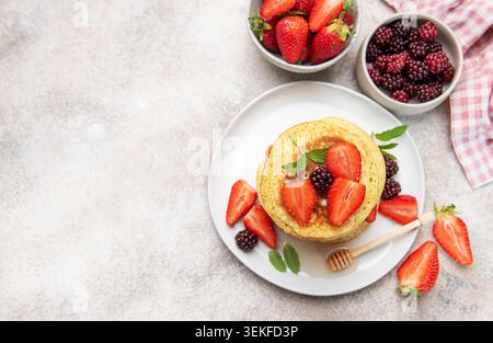 Stapel Pfannkuchen mit frischen Erdbeeren, Brombeeren, Honig und Minzblättern auf einem Teller Stockfoto